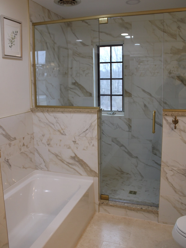 Closeup photo of remodeled bathroom tub and shower area with gold accents, completed by Lenawee Home Design